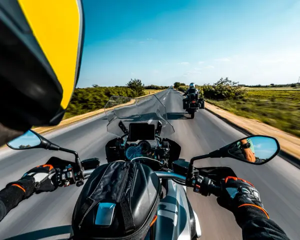 Przełęcz Salmopolska widziana z perspektywy motocyklisty. Droga wijąca się pośród zielonych pól, błękitne niebo i inny motocykl przed nami.