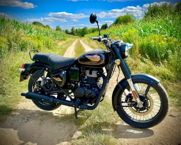 Czarny motocykl Royal Enfield Diesel na polnej drodze, otoczony zielenią i kukurydzą.