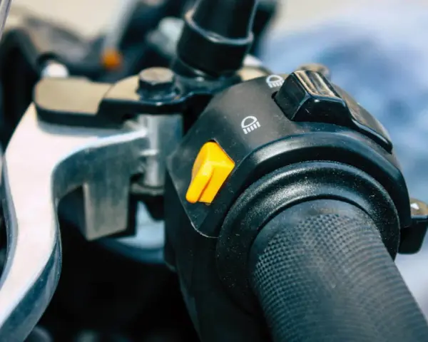 Pomarańczowy przycisk na kierownicy motocykla, który może służyć jako kill switch, obok przełącznika świateł.