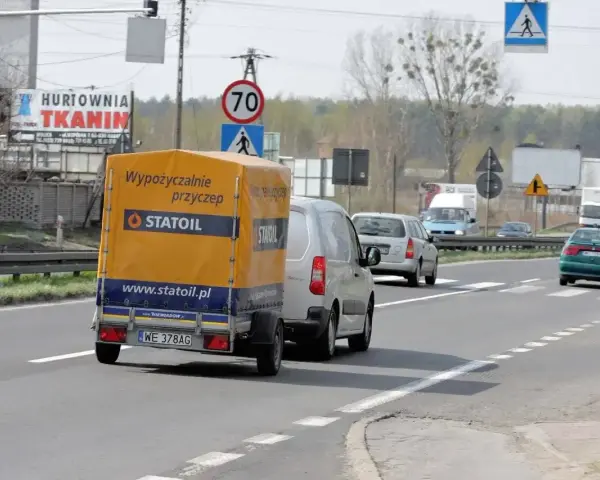 Samochód z przyczepą Statoil jedzie drogą. Znak ograniczenia prędkości 70 km/h sugeruje, ile można jechać na autostradzie w tym miejscu.