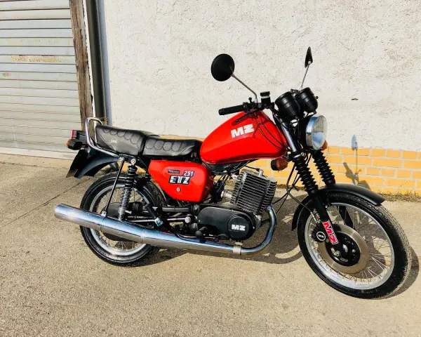 Czerwony motocykl MZ ETZ 251 z lat 80. stoi przed garażem.