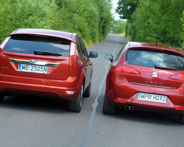 Dwa czerwone auta jadą drogą. Jedno z nich, Ford Focus, próbuje omijanie, podczas gdy Seat Leon wykonuje wymijanie.