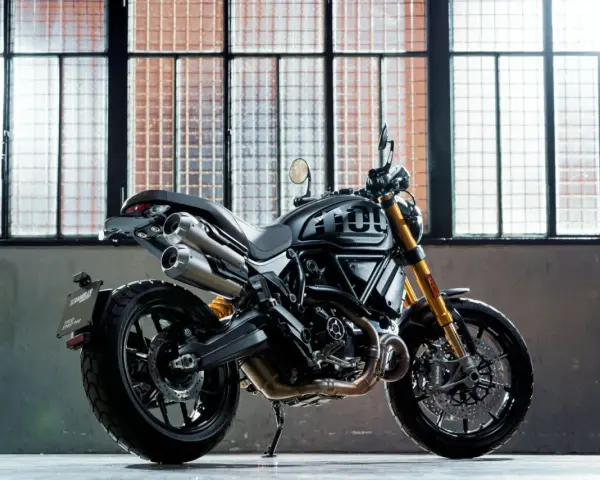 Czarny motor scrambler z podwójnym wydechem i złotym zawieszeniem, gotowy do jazdy po miejskich ulicach.