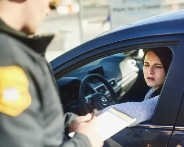 Policjant wręcza kobiecie w samochodzie mandaty w Austrii. Kobieta wygląda na zmartwioną.