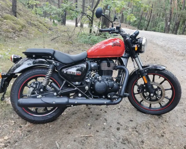 Czerwony Royal Enfield Meteor 350 na leśnej drodze. Klasyczny wygląd i gotowość do podróży.