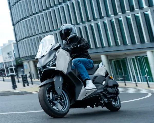 Mężczyzna w kasku jedzie skuterem Yamaha X-MAX 125 po mieście. Czy to lepszy wybór niż Honda Forza 125?