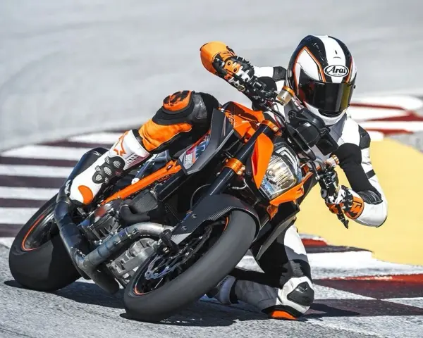 Motocyklista w kombinezonie ściga się na torze na pomarańczowym KTM 1290 Super Duke, pochylony w zakręcie.