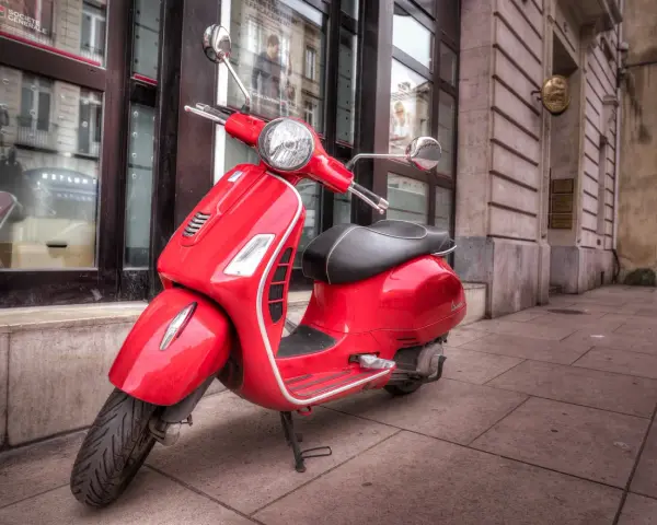 Czerwony skuter Vespa, idealny do miasta. Marzenie o posiadaniu go jest jak marzenie o zdobyciu prawa jazdy na skuter.