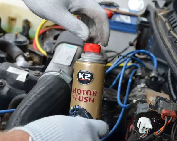 Ręka w rękawiczce trzyma puszkę płukanki do silnika motocyklowego K2 Motor Flush, gotowa do użycia w silniku.