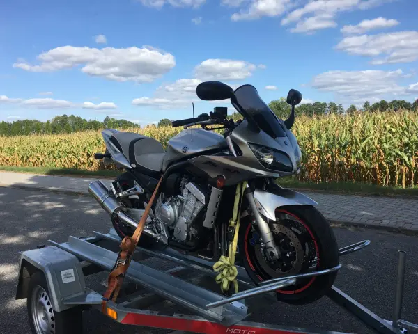 Srebrny motocykl Yamaha na przyczepce, gotowy do rejestracji z Niemiec. W tle pole kukurydzy i błękitne niebo z chmurami.