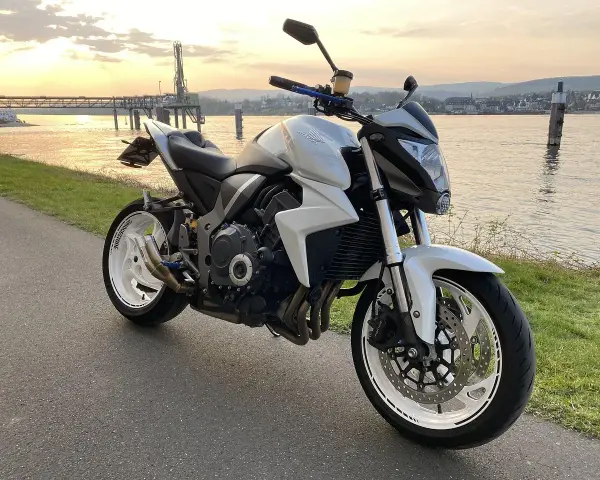 Biały motocykl Honda z silnikiem 35 kw nad rzeką o zachodzie słońca.