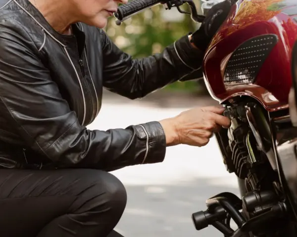 Kobieta w skórzanej kurtce sprawdza regulator napięcia w motocyklu.