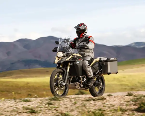 Motocyklista w kasku i stroju podróżuje na motocyklu BMW 800 GS po piaszczystej drodze, w tle górzysty krajobraz.