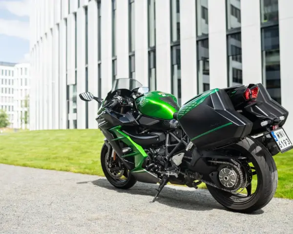 Zielony Kawasaki Ninja H2 z czarnymi kuframi, gotowy do podróży obok nowoczesnego budynku.