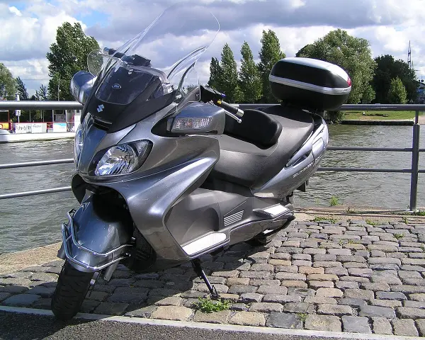 Szary Suzuki Burgman 650, gotowy na podróż w stylu V-max, stoi nad wodą.