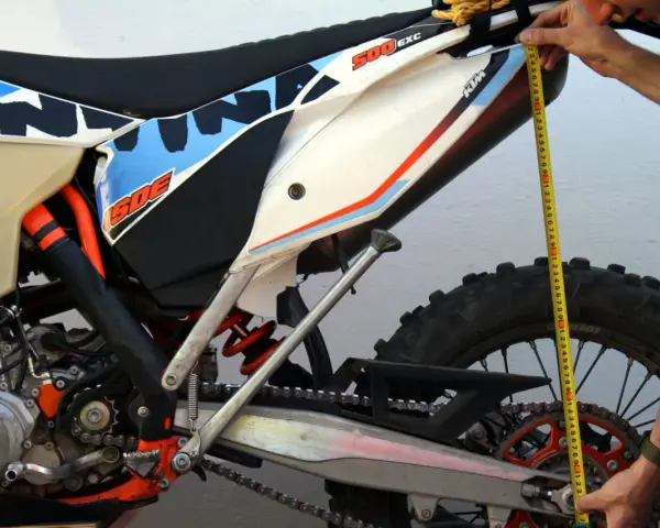 Mierzenie preload w amortyzatorze motocykla KTM 500 EXC. Dłoń trzyma miarkę przy tylnym kole.