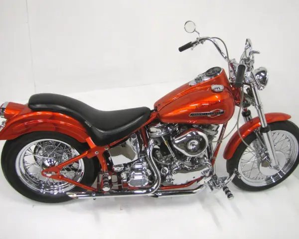 Pomarańczowy motocykl Harley-Davidson z silnikiem panhead, błyszczący chrom i płomienie na baku.