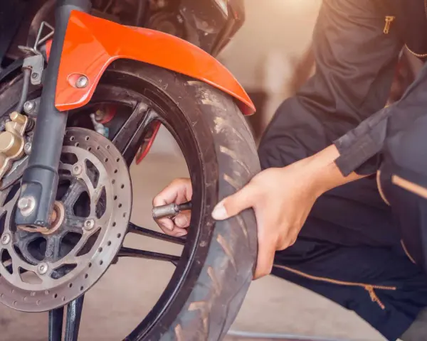 Mechanik sprawdza ciśnienie w oponie motocykla. Dowiedz się, jaka jest wymiana opon motocyklowych cena.