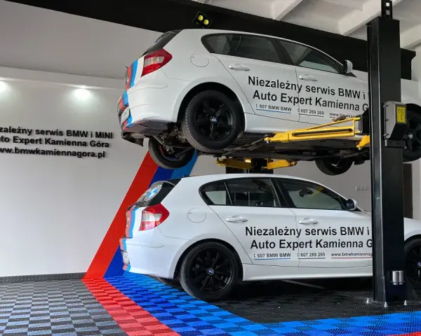 Dwa białe BMW, jedno na podnośniku, w serwisie Auto Expert. W tle logo BMW.