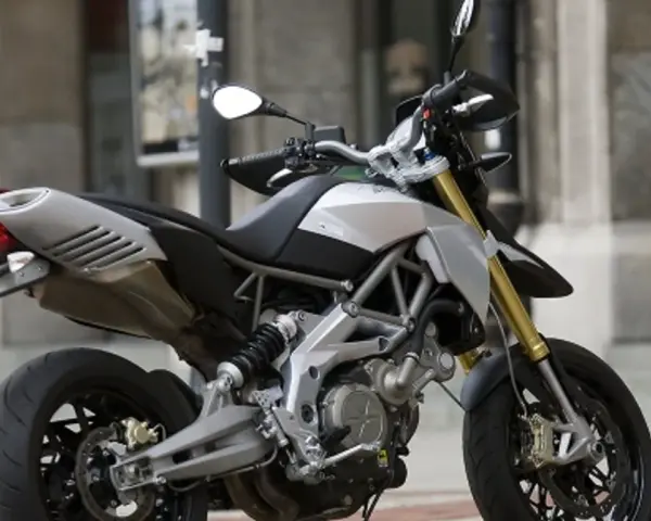Srebrno-czarny motocykl Aprilia Dorsoduro 750 z żółtymi amortyzatorami, gotowy do jazdy po miejskich ulicach.