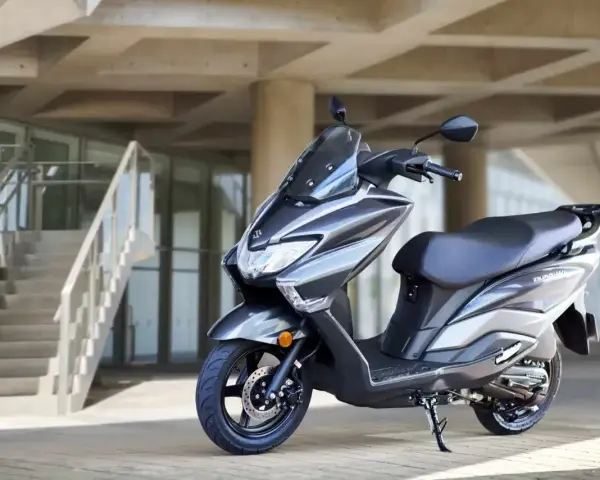 Szary skuter Suzuki Burgman 125 na tle nowoczesnego budynku z betonowymi schodami.