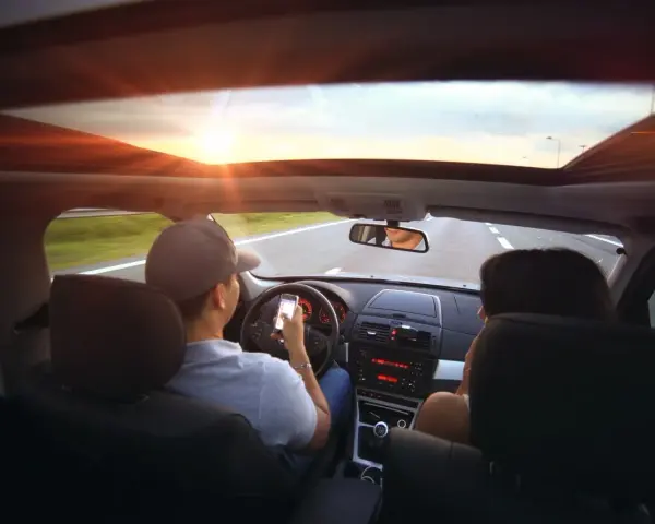 Kierowca z telefonem w ręku, pasażerka obok. Zasada ograniczonego zaufania w praktyce, bo kto wie, co na ekranie?