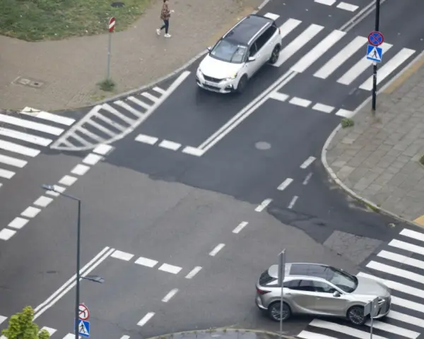 Skrzyżowanie dróg z przejściami dla pieszych i samochodami. Jeden biały SUV i srebrny crossover czekają na zielone światło.