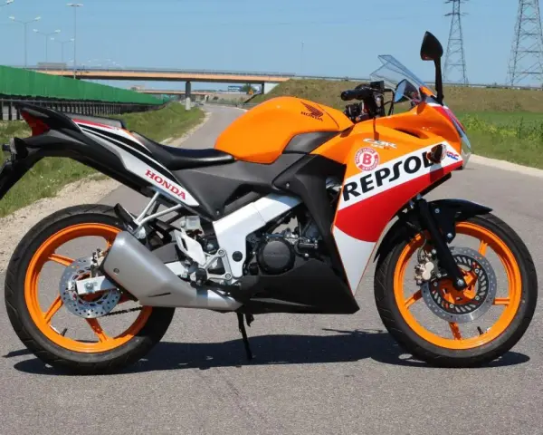 Pomarańczowy motocykl Honda CBR 125 Repsol na drodze. Warto sprawdzić honda cbr 125 dane techniczne przed zakupem.