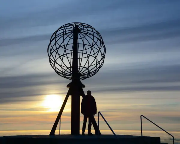 Sylwetka człowieka przy globusie na Nordkapp podczas zachodu słońca.