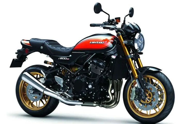 Stylowy czarny motocykl Kawasaki Z900RS z pomarańczowo-żółtym malowaniem na baku i złotymi felgami.