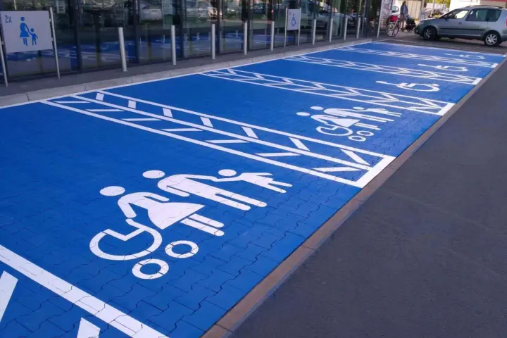 Niebieski parking z białymi symbolami osób na wózkach inwalidzkich i rodzin. Znak P19 informuje o przeznaczeniu miejsc.