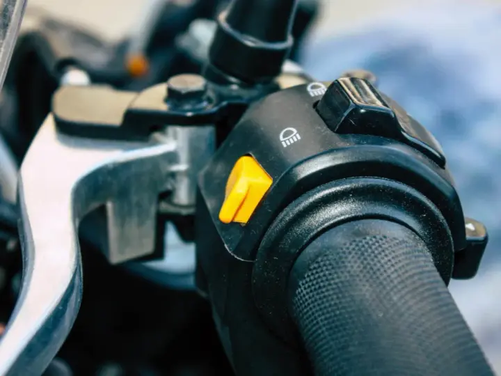 Pomarańczowy przycisk na kierownicy motocykla, który może służyć jako kill switch, obok przełącznika świateł.