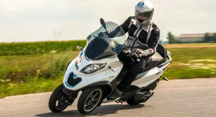 Biały Piaggio MP3 500 z kierowcą w kasku pędzi po drodze. Zastanawiasz się nad jego spalaniem?