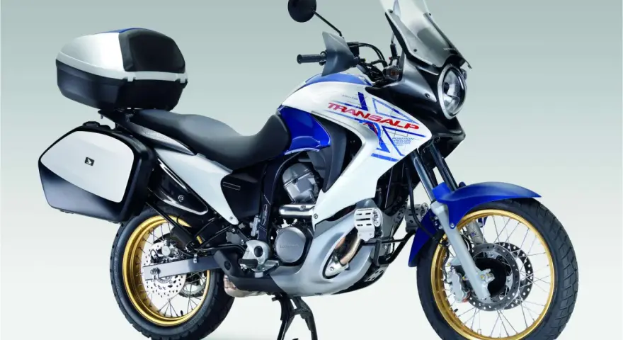 Honda Transalp 700 dane techniczne: turystyczny motocykl z kuframi, biało-niebieski, złote felgi, gotowy na przygodę.