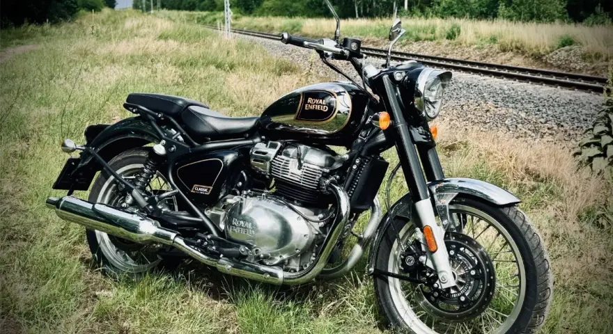 Czarny Royal Enfield Classic 650 lśni chromem na tle torów kolejowych i zieleni. Gotowy na przygodę.