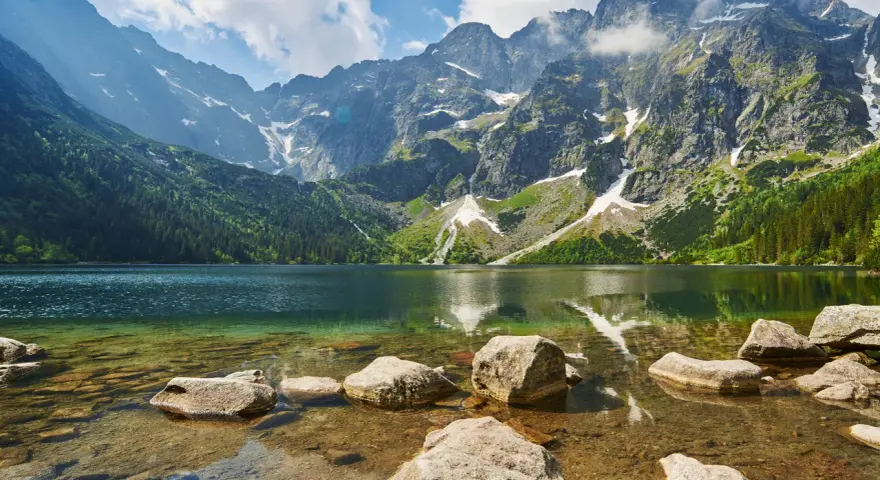 Kamienista droga na Morskie Oko prowadzi przez malownicze Tatry. Jezioro odbija skaliste szczyty i zielone lasy.