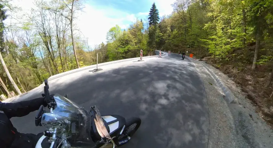 Motocyklista pokonuje zakręty na malowniczej drodze stu zakrętów, otoczonej zielonymi lasami.