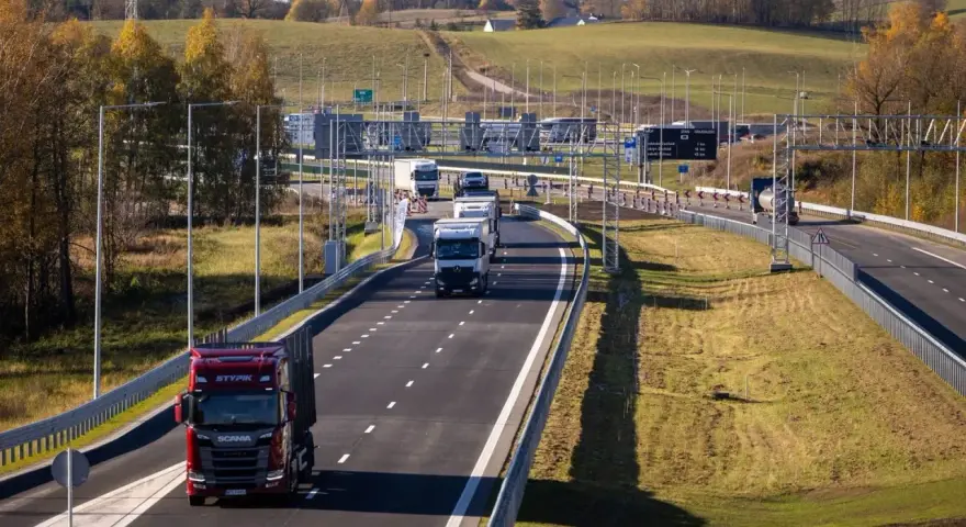 Ciężarówki na Via Baltica w jesiennym krajobrazie. Droga szybkiego ruchu z wieloma pojazdami, w tym czerwonym Scanią.