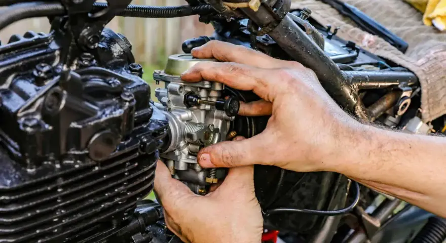 Dłonie mechanika regulują gaźnik motocykla, kluczowy element odpowiedzialny za symbol ssania paliwa i powietrza.