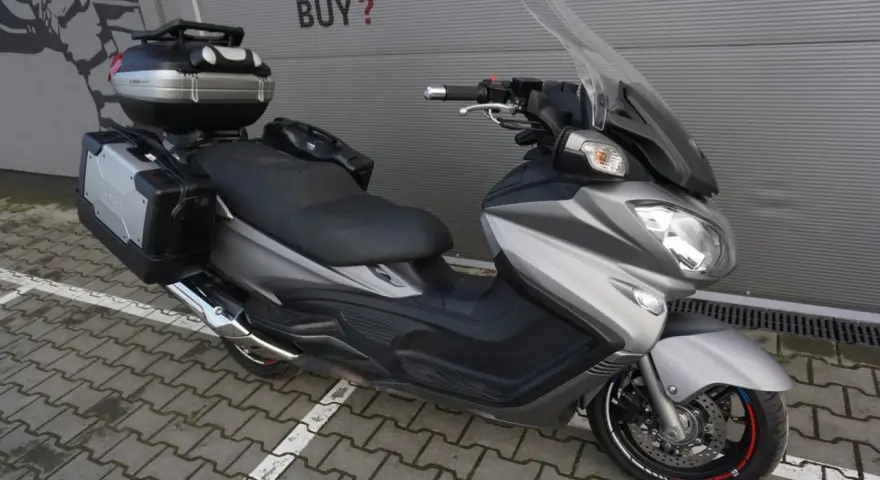 Srebrny Suzuki Burgman 650 Executive z kuframi, gotowy na dalekie podróże.