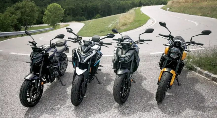 Cztery motocykle typu naked stojące na zakręcie górskiej drogi.