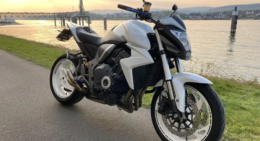 Biały motocykl Honda CB1000R, model a2 motor, zaparkowany nad rzeką o zachodzie słońca.