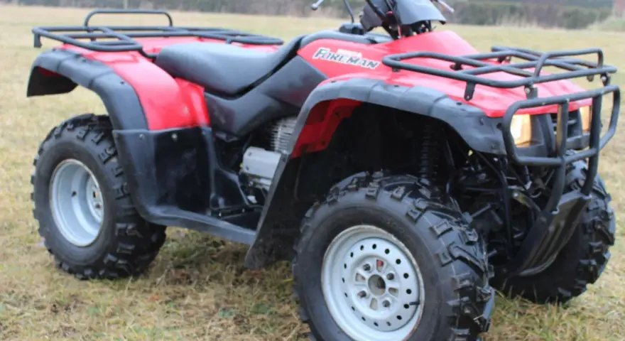 Czerwony quad Honda TRX 350 Foreman gotowy do jazdy po nierównym terenie.