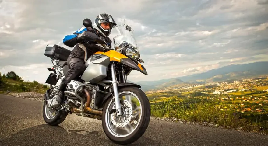 Motocyklista w kasku jedzie na motocyklu turystycznym. W tle rozciąga się malowniczy krajobraz z miastem. Zastanawiasz się nad koszt przerejestrowania motocykla?