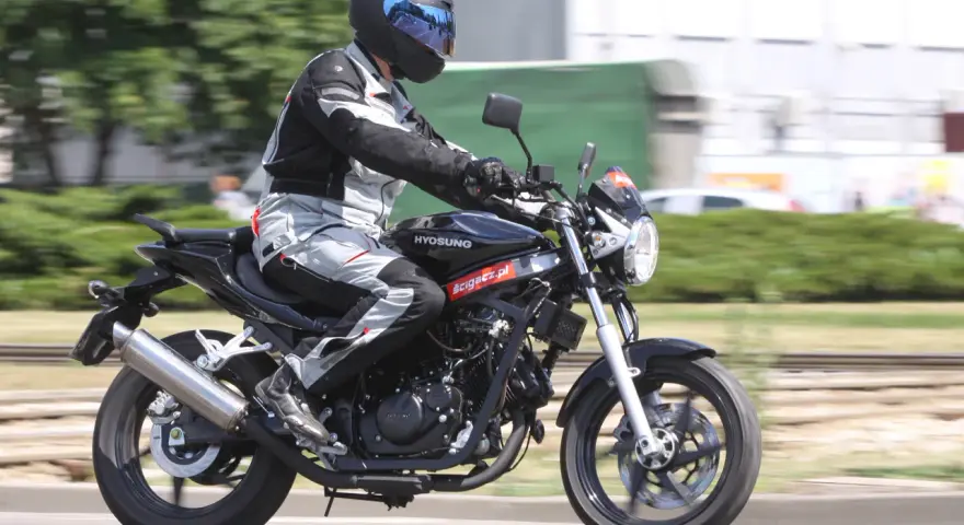 Motocyklista w kasku i kombinezonie jedzie na czarnym motocyklu Hyosung GT 125.