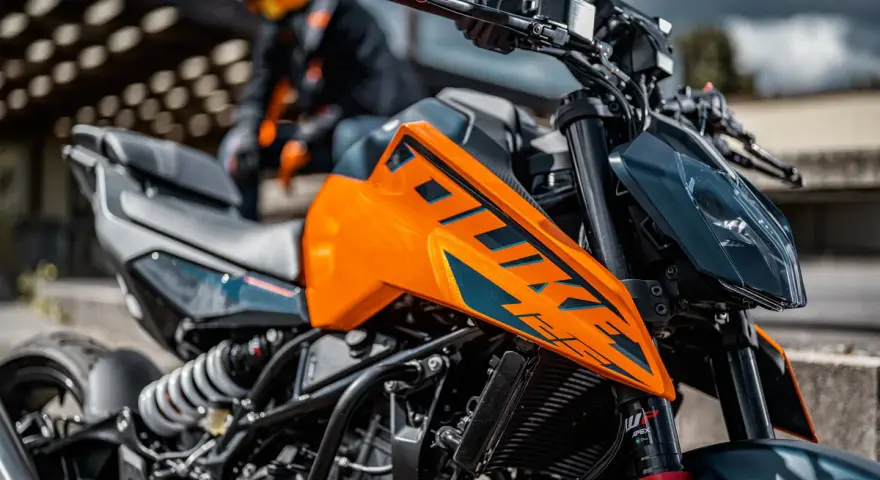 Pomarańczowy KTM Duke 390, zarejestrowany na 125, z motocyklistą w tle. Gotowy na przygodę!