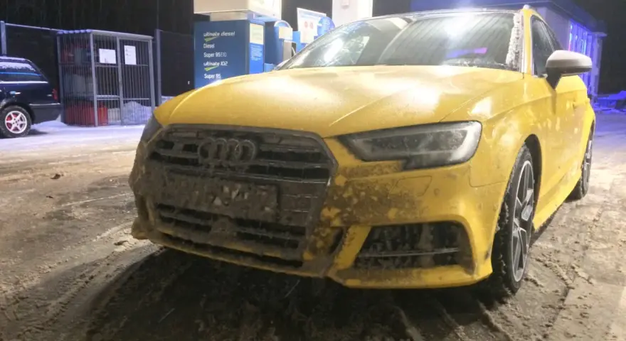 Żółte Audi na stacji benzynowej, pokryte błotem i śniegiem. Nieczytelna tablica rejestracyjna utrudnia identyfikację.