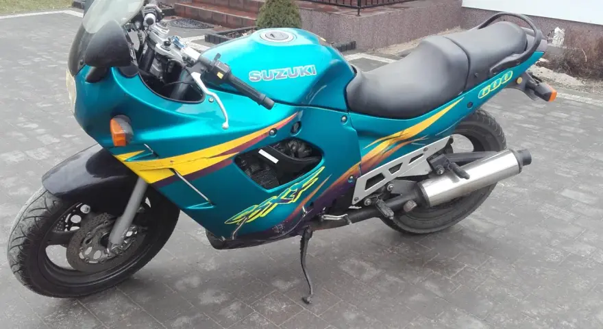 Turkusowy Suzuki GSXF 600 z żółto-fioletowymi grafikami, zaparkowany na kostce brukowej przed domem.
