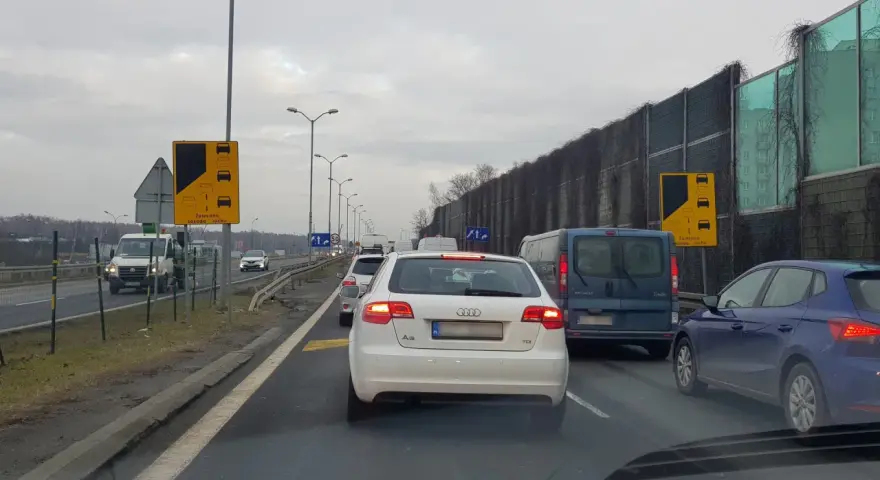 Korek na drodze, znaki informują o zalecanej zasadzie ruchu "na suwak". Unikaj mandatu, stosuj się do przepisów.