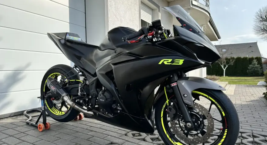 Czarny motocykl Yamaha R3 z żółtymi akcentami na felgach i owiewkach. Widać sportowy wydech Yoshimura. Idealny do poznania yamaha r3 dane techniczne.